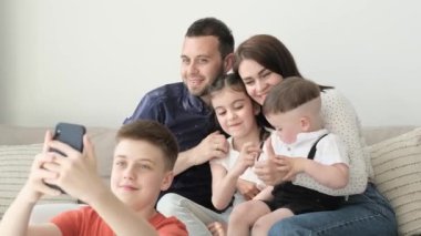 Happy, smiling family sitting on sofa in living room. Son, teenage boy taking selfie with his family