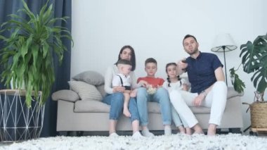 A family with three children watching a movie sitting on a sofa in the living room. Dad turns on the TV. Family time together