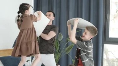 Family time dad with kids. A father, daughter and two sons are fighting over pillows in the living room