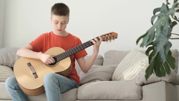 Teenage Boy Plays Guitar While Sitting Sofa Bright Room Learning — Αρχείο Βίντεο