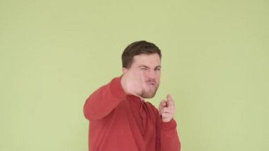 Handsome young man in a red sweater funny shows shots from a gun with his hands isolated on the background in the studio, a man shows his great mood on camera