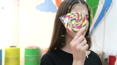 Smiling teenage girl in a black T-shirt with a lollipop on a white background. Girl with a big candy in her hands