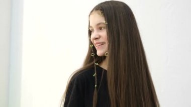 A teenage girl poses in front of the camera, she laughs and straightens her long hair. Baby on a white background in the studio, girl 12 years old, model school