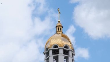 Golden dome of the church on a background of blue sky. The top of the bell tower on a background of sky. Birds in the sky