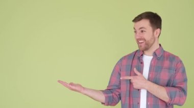 Caucasian man pointing finger at copy space isolated on yellow and green background. A young handsome man demonstrates an idea or advertises something