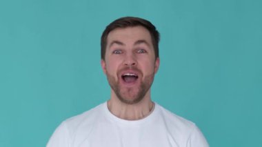 Handsome guy with a wow expression. Close up of young man posing on blue background. Portrait of a smiling european man who raises his thumbs up