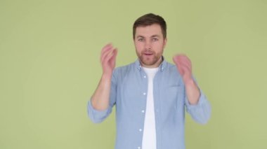 European young man in casual blue denim shirt looking shocked, surprised wow showing hands head blast brain isolated on yellow green studio background. An explosion of emotions in a man