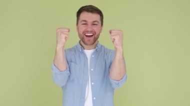 Handsome smiling american man in denim shirt white t-shirt isolated on yellow-green background in studio. the man rejoices and raises his hands