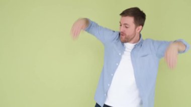 Happy american man in denim shirt funny dancing isolated on yellow and green background in studio. the man rejoices and raises his hands