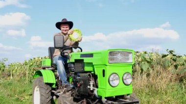 Male agronomist near a sunflower plantation, he is sitting in a tractor and having fun, funny man, farmer, joking, smiling, joyful man