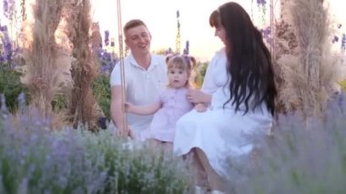 Beautiful young family mom and dad with daughter in nature, happy family on a swing. Happy family concept.
