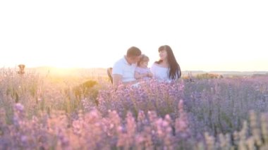 Beautiful young family dad and mom with little girl sitting on picnic at sunset in lavender field. Concept of happy family relations.