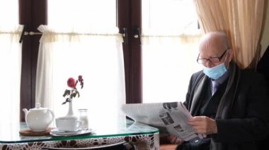 The waiter serves in the cafe, he brings his grandfather coffee. Gray-haired grandfather is resting in a cafe and reading a newspaper