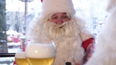 Friends in Santa Claus costumes are having fun at a New Years party, drinking beer in a pub. Celebration of Christmas and New Year 2023