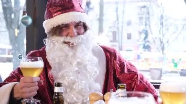 Friends in Santa Claus costumes are having fun at a New Years party, drinking beer in a pub. Celebration of Christmas and New Year 2023