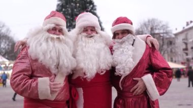 Portrait of happy senior men in costumes of Santa Claus on the background of the Christmas tree. Santa greets passers-by. Christmas mood concept