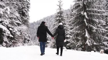 Young people in love, a boy and a girl, walking on a winter road in the middle of snow-covered trees. Winter background