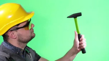 Male builder in yellow helmet and goggles working with hammer, on green background chromakey, goggles for construction worker
