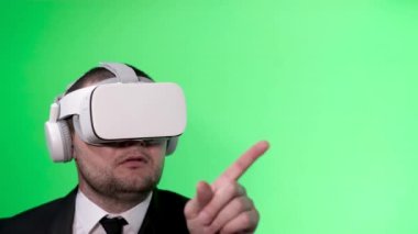 A man in a black suit uses virtual reality goggles. VR. Green background. The office worker uses a virtual interface. Movement of hands on a green background chromakey.