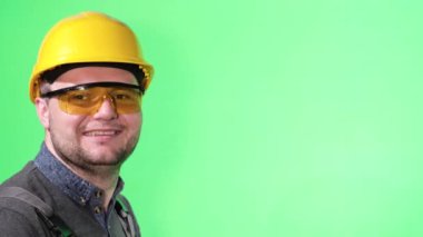Young engineer in a protective helmet on a background of chromakey. Portrait of an engineering worker, he looks at the camera and laughs
