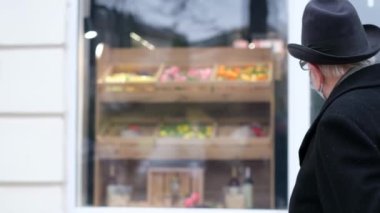 The poor grandfather looks at the shop window, he has no money for groceries. Homelessness in old age. Upset old pensioner