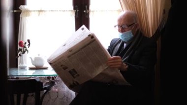Gray-haired grandfather with glasses reads a fresh newspaper and drinks coffee while sitting in a restaurant. Press news