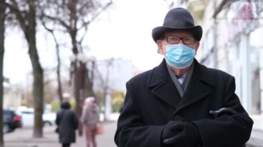 An old grandfather in a mask against viruses, he walks the streets of a European city. Threat of influenza virus infection. Coronavirus pandemic