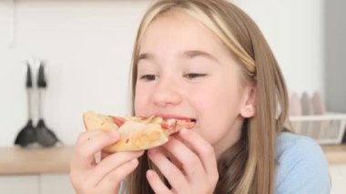 Video of pretty girl eating pizza on kitchen background. Girl with colored strands of hair