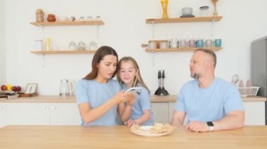 Family shooting in the studio in the kitchen. Mom takes pictures of pizza. Happy family together