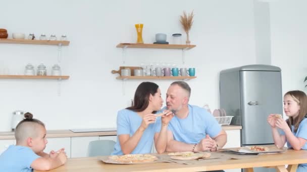 Family Four Sitting Kitchen Table Eating Pizza Mom Dad Kissing — Video Stock