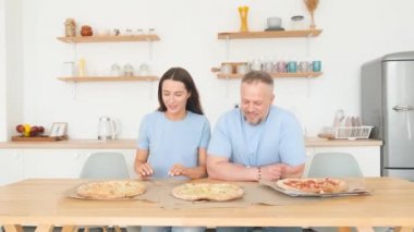 Happy parents kissing in the kitchen. The whole family tastes pizza. Family image in blue t-shirts. Happiness concept