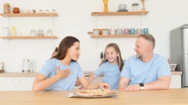 Positive family in their cozy kitchen. Hungry children eat pizza. Mom, dad, daughter and son