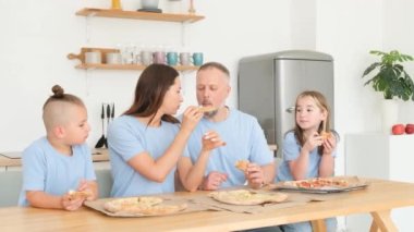 Family video of a family sitting in the kitchen eating delicious pizza. Mom gives a piece of pizza to Dad