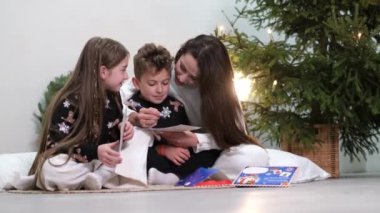 Mom reads a fairy tale to children before bed on New Years Eve. Happy family on New Years Eve, on the background of the Christmas tree. Christmas comfort in the house