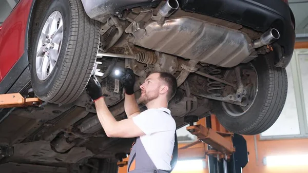 A professional car mechanic works under the king of a hoisting machine in a car repair shop. Car service, repair of electric cars