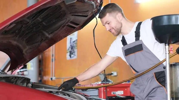A mechanic man makes an oil change in a car. The concept of automotive automotive service. The work of a car mechanic