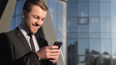 Portrait cheerful businessman using smartphone at modern street. 