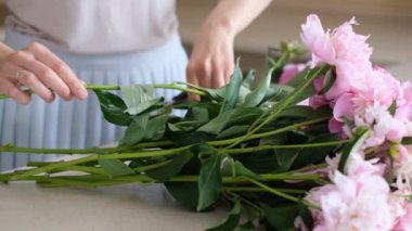 Woman, florist put a peonies in a vase. Beautiful pink pions peonies in a jar. Close up.