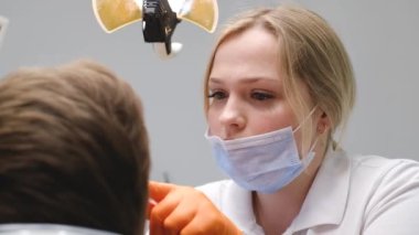 Young blonde dentist treats the teeth of a young guy. Modern and painless dental treatment
