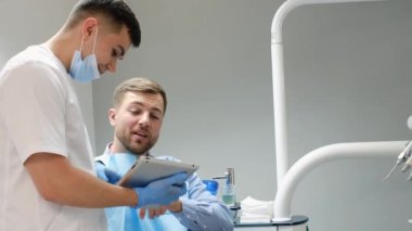 A young patient of European appearance is sitting in a dental chair and talking to a dentist. Modern treatment of dental diseases
