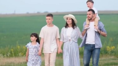Loving parents and children walk along the field, holding hands. Happy family on the background of green grass and sky. Together Forever.