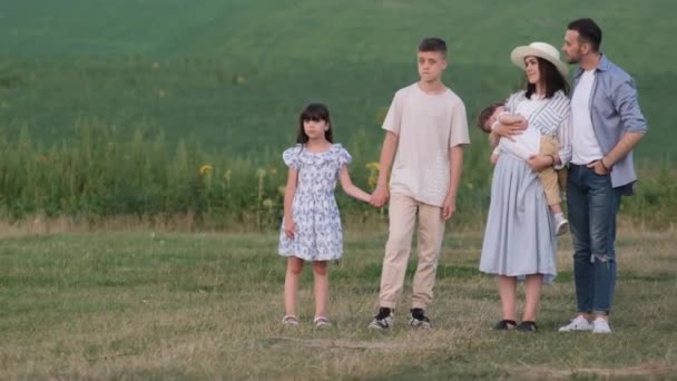 A big friendly American family is standing in a field in the middle of green grass. A family with three children. Family photo session in nature.
