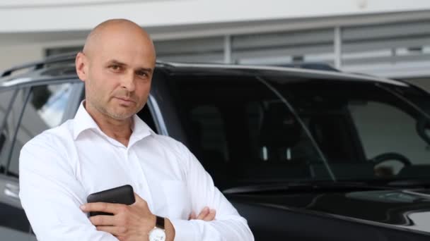 一位穿着白衬衫的秃头中年男子站在车库里一辆汽车的后面 卖车的销售经理 — 图库视频影像