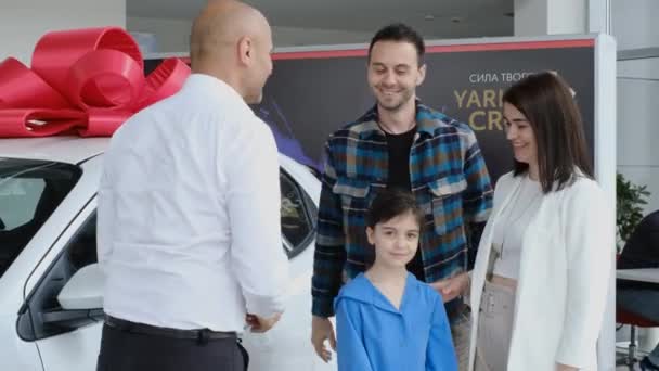 卖家祝贺这家人买了一辆新车 在汽车经销店里的快乐家庭 一辆红色蝴蝶结的新家用轿车 — 图库视频影像