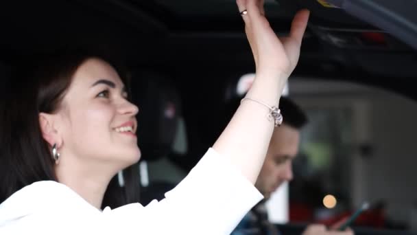 車内には幸せで満足した女が座って鏡を見ている 車を買う 車の販売代理店で家族のカップル 自動車事業 — ストック動画