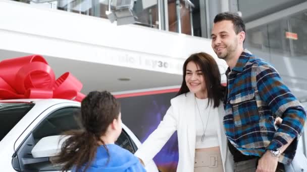一个有两个孩子的快乐家庭买了一辆新车 购买的喜悦 一辆有红色蝴蝶结的车快乐的拥抱 — 图库视频影像