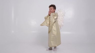 Küçük çocuk, stüdyoda beyaz kanatlı beyaz bir melek şeklinde dua ediyor. 4k video