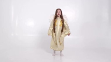 Beyaz kanatlı, melek şeklinde küçük bir kız stüdyoda beyazlar üzerinde oynuyor. 4k video