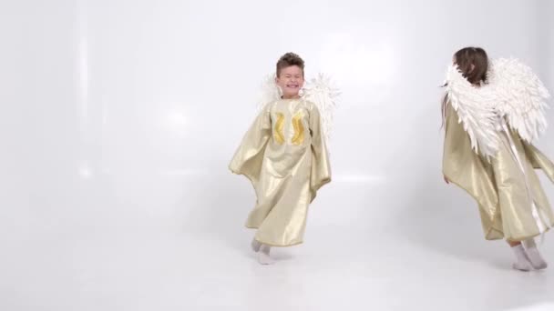 スタジオの白い背景に白い翼を持つ子供天使がスタジオで遊んでいます 4Kビデオ — ストック動画