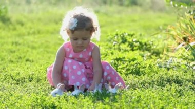 Pembe elbiseli bir çocuk bahçede beyaz tavşanlarla oynuyor. Evcil hayvanları olan mutlu bir çocuk. Küçük tavşanlar